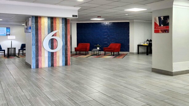 A lobby with a large number '6' sign, a blue wall, red chairs, and a small table with a plant. - 1 King Bed | Suite, Non-Smoking, Micfridge (Columbus)