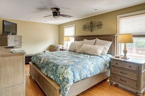 Quarto com cama, mesas de cabeceira, penteadeira, ventoinha no teto e televisão sobre um móvel.