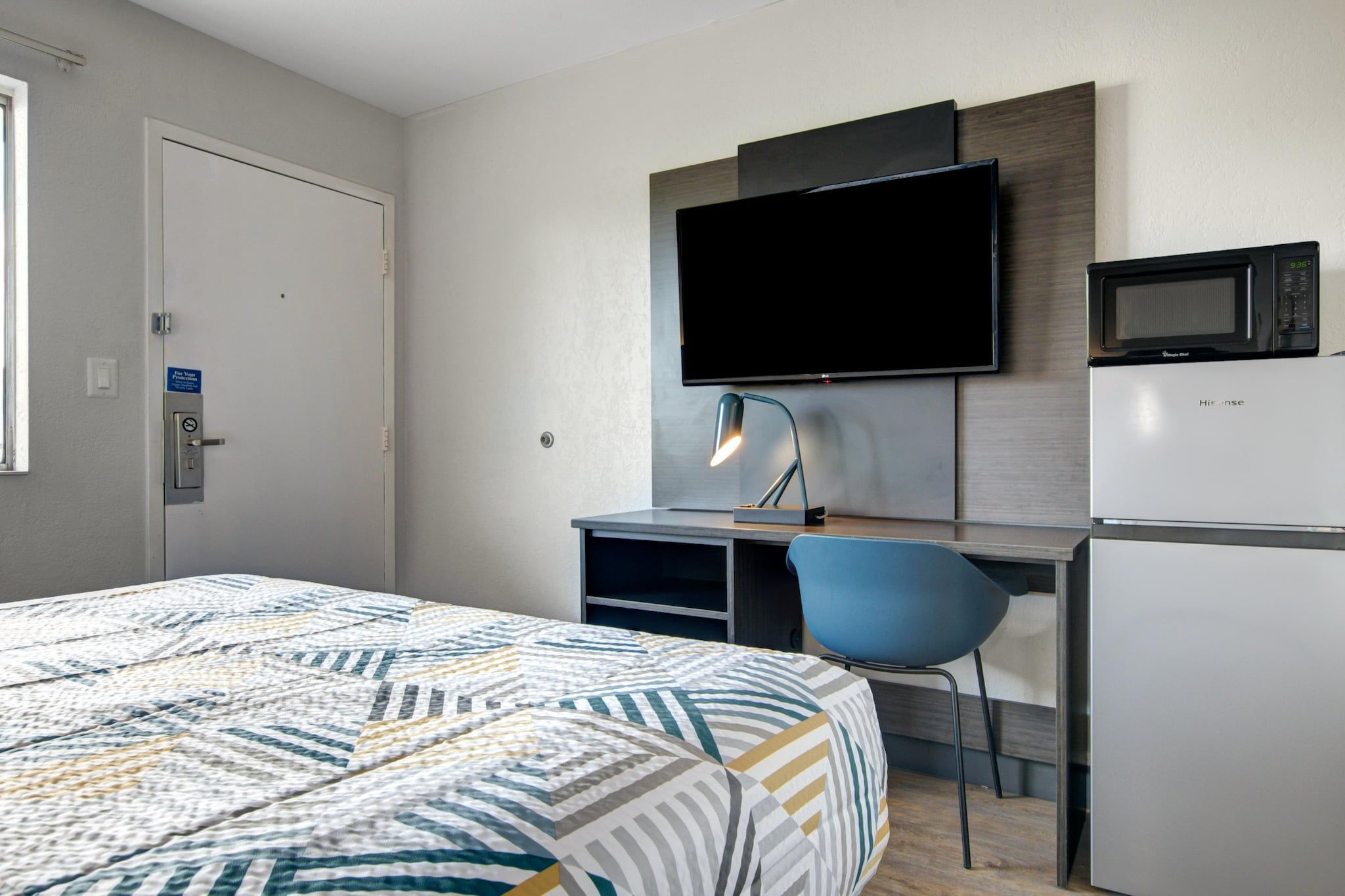 A hotel room with a bed, a desk with a chair, a television, a microwave, and a refrigerator.