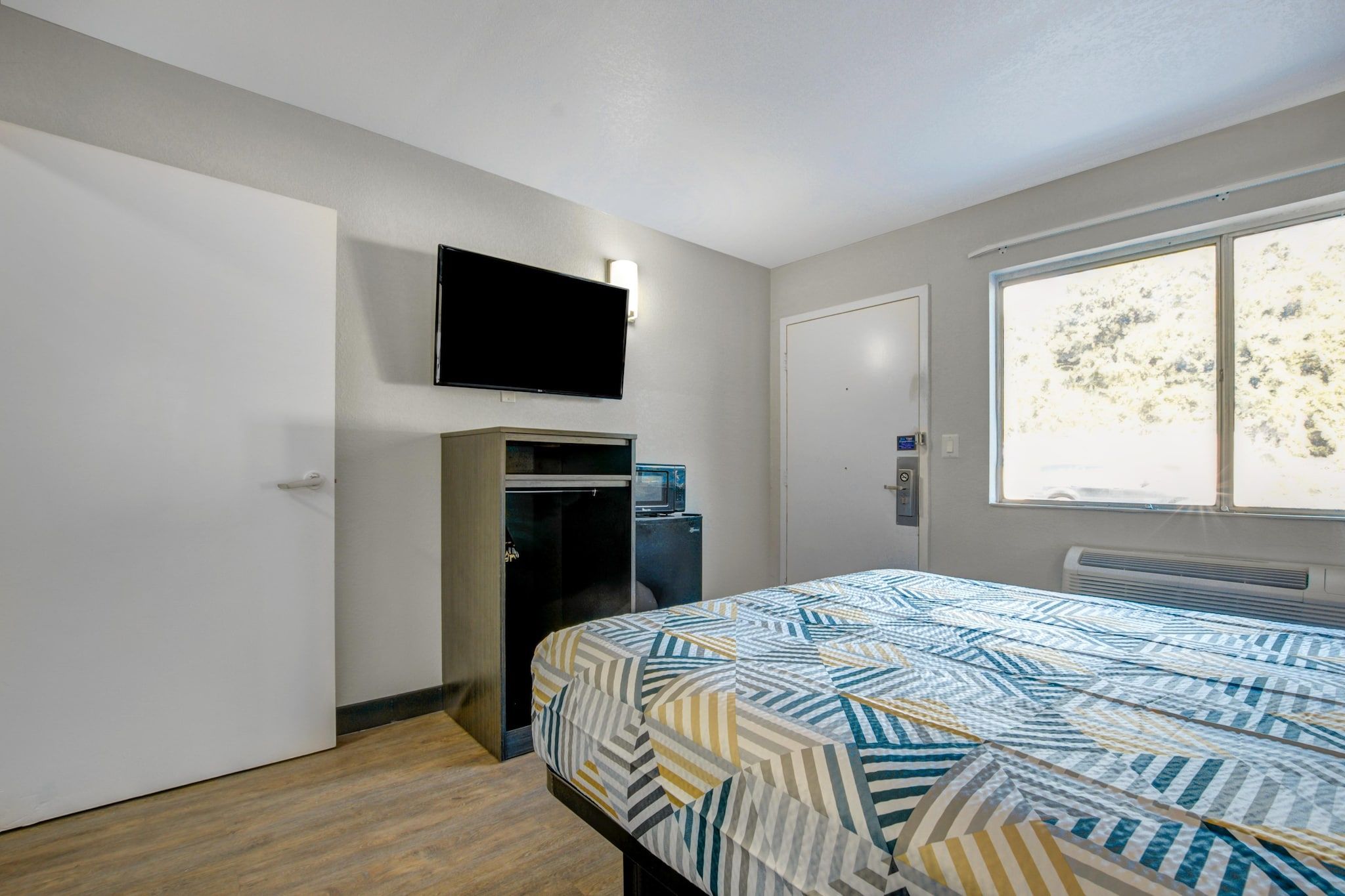 Een slaapkamer met een bed, een aan de muur bevestigde televisie, een deur en een raam.