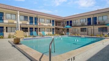 A pool area with a diving board, lounge chairs, and a building with multiple balconies.