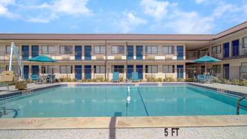 A hotel with a swimming pool, outdoor seating, and a multi-story building.