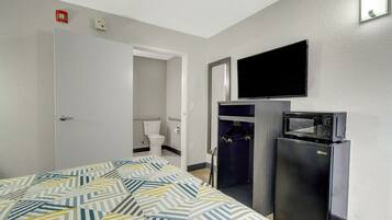 Una habitación de hotel con cama, televisión, refrigerador y baño.