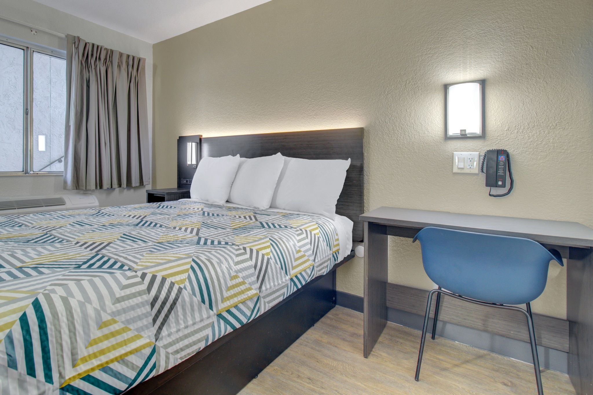 Een hotelkamer met een bed, een bureau, een stoel, een telefoon en een raam met gordijnen.