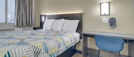 Ett hotellrum med en säng, ett skrivbord, en stol, en telefon och ett fönster med gardiner.