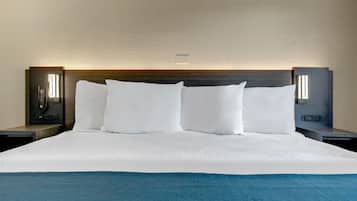 Een hotelkamer met een groot bed, witte beddengoed en een blauwe plaids. Twee nachtkastjes met lampen en een aan de muur bevestigd telefoon.