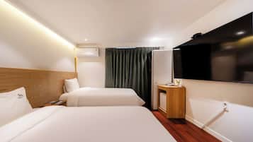 A hotel room with two beds, a flat-screen TV, a bedside table with a phone, and a wall-mounted air conditioning unit.
