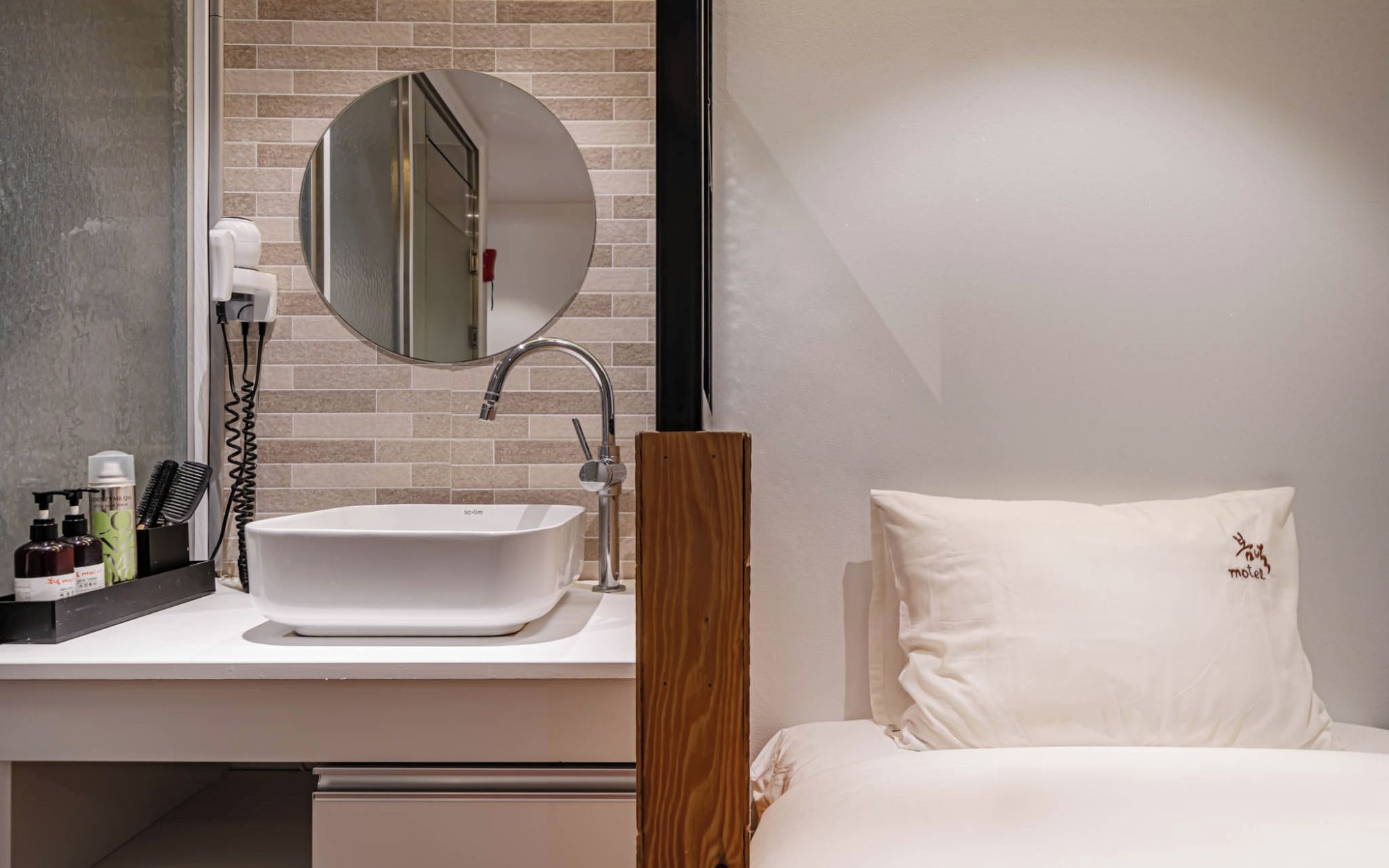 Un baño moderno con un lavamanos blanco, un espejo redondo y artículos de tocador sobre la encimera.