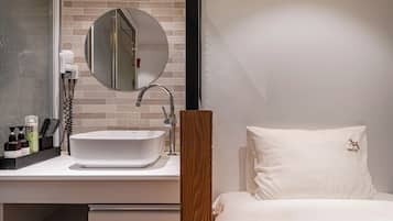 Un baño moderno con un lavamanos blanco, un espejo redondo y artículos de tocador sobre la encimera.