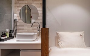 Ein modernes Badezimmer mit einem weißen Waschbecken, einem runden Spiegel und Pflegeprodukten auf der Ablagefläche.