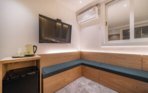 A compact room with a built-in bench, a wall-mounted TV, and a window with an air conditioning unit. - Busan Suyeong Bomnal (Busan)