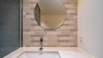A bathroom with a white sink, a round mirror, and beige tiled walls.