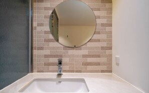 A bathroom with a white sink, a round mirror, and beige tiled walls. - Busan Suyeong Bomnal (Busan)