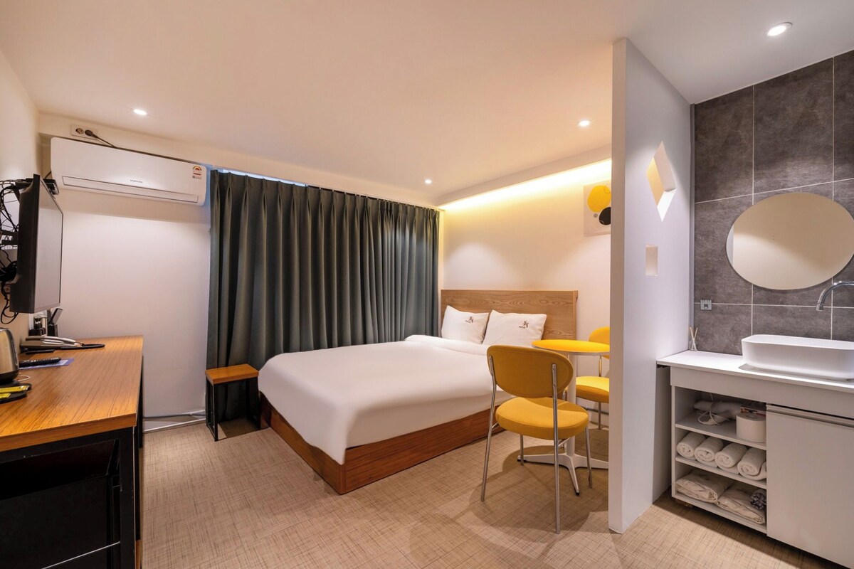 A hotel room with a bed, a desk, a chair, a bathroom with a sink and mirror, and a wardrobe.