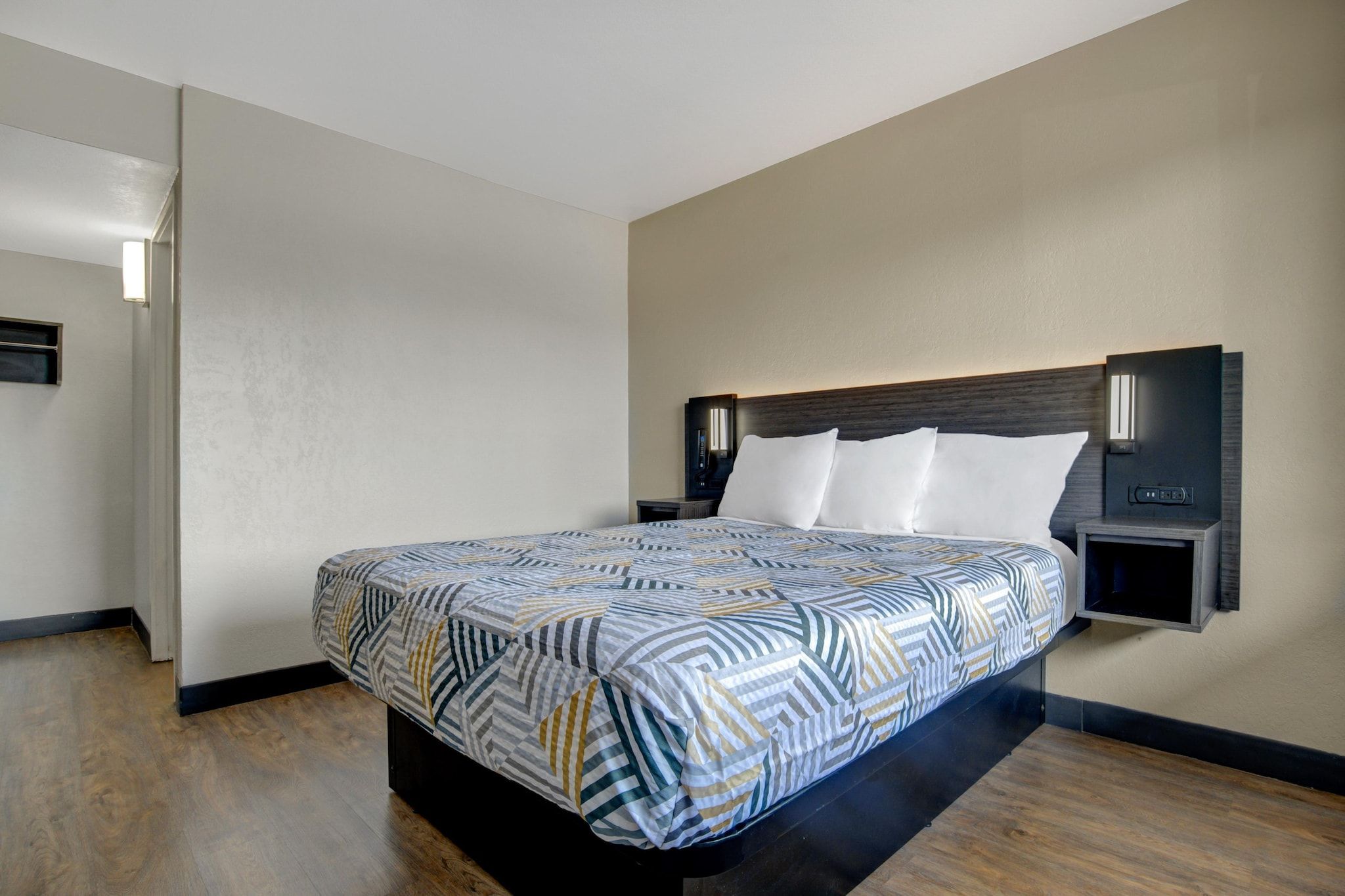 Een hotelkamer met een groot bed, een nachtkastje, een aan de muur bevestigde televisie en een modern hoofdeinde.