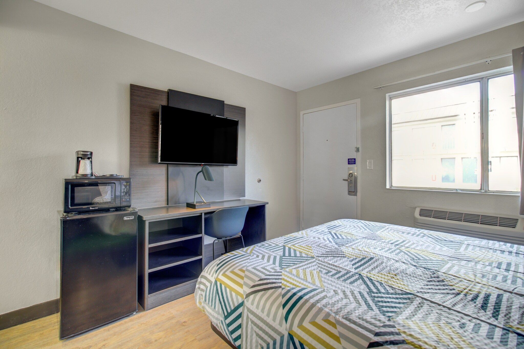 A bedroom with a bed, a desk with a computer, a television, and a window with a view.