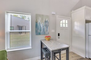 A room with a window, a door, a table with a bowl of snacks, and a painting on the wall. - Stylish Tiny Home: 6 Mi to Gladewater Antiquing! (Gladewater)