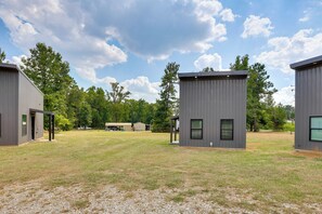 A modern building complex with multiple units, a grassy field, and trees in the background. - Stylish Tiny Home: 6 Mi to Gladewater Antiquing! (Gladewater)