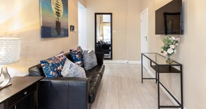A modern living room with a leather sofa, decorative pillows, a glass coffee table, and a wall-mounted TV. - South Kensington Base Near Knightsbridge (London)