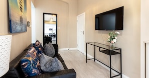 A living room with a sofa, a coffee table, a flat-screen TV, and a painting on the wall. - South Kensington Base Near Knightsbridge (London)