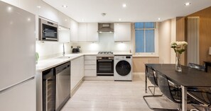 A modern kitchen with built-in appliances, a dining area with a table and chairs, and a window with a view. - South Kensington Base Near Knightsbridge (London)