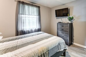 A bedroom with a bed, a dresser, a television mounted on the wall, and a window with curtains. - Quiet Cul-De-Sac Near Fort Benning, Columbus (Columbus)