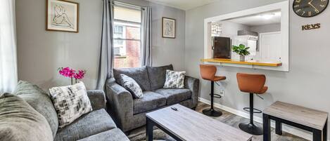 A modern living room with grey sofas, a wooden coffee table, and a bar area with stools.