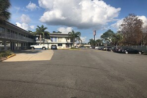 Un parking avec un bâtiment sur la gauche et un panneau sur la droite.