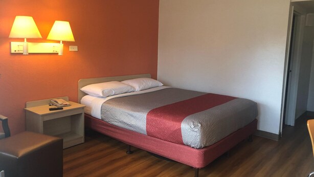 Una habitación de hotel con cama, mesitas de noche, teléfono y lámparas de pared.