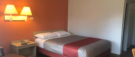 Una habitación de hotel con cama, mesitas de noche, teléfono y lámparas de pared.