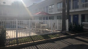 Un patio con cerca blanca, mobiliario exterior y un paraguas rojo.