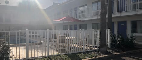 A courtyard with a white fence, outdoor furniture, and a red umbrella.