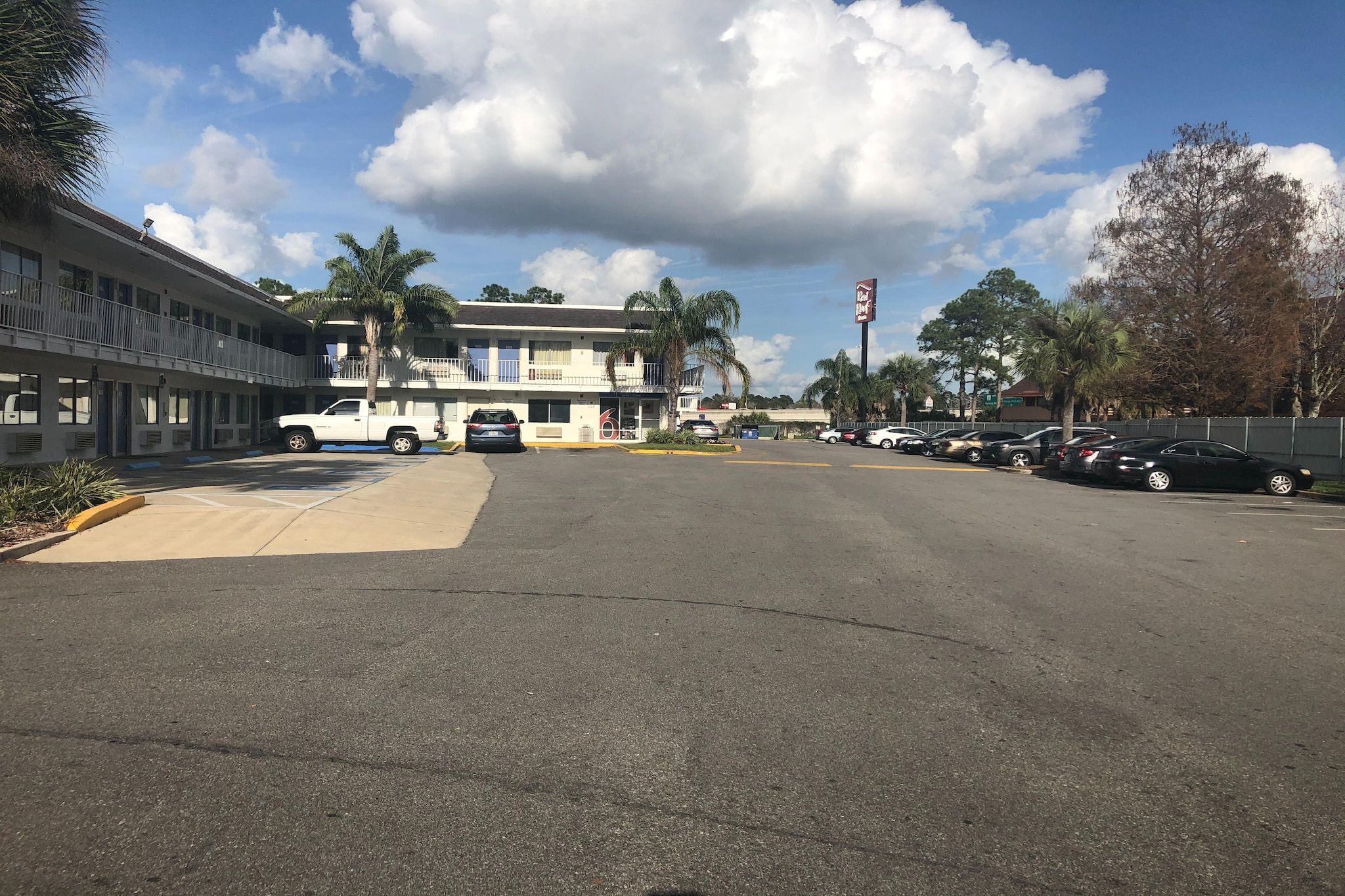 A parking lot with a building on the left and a sign on the right.