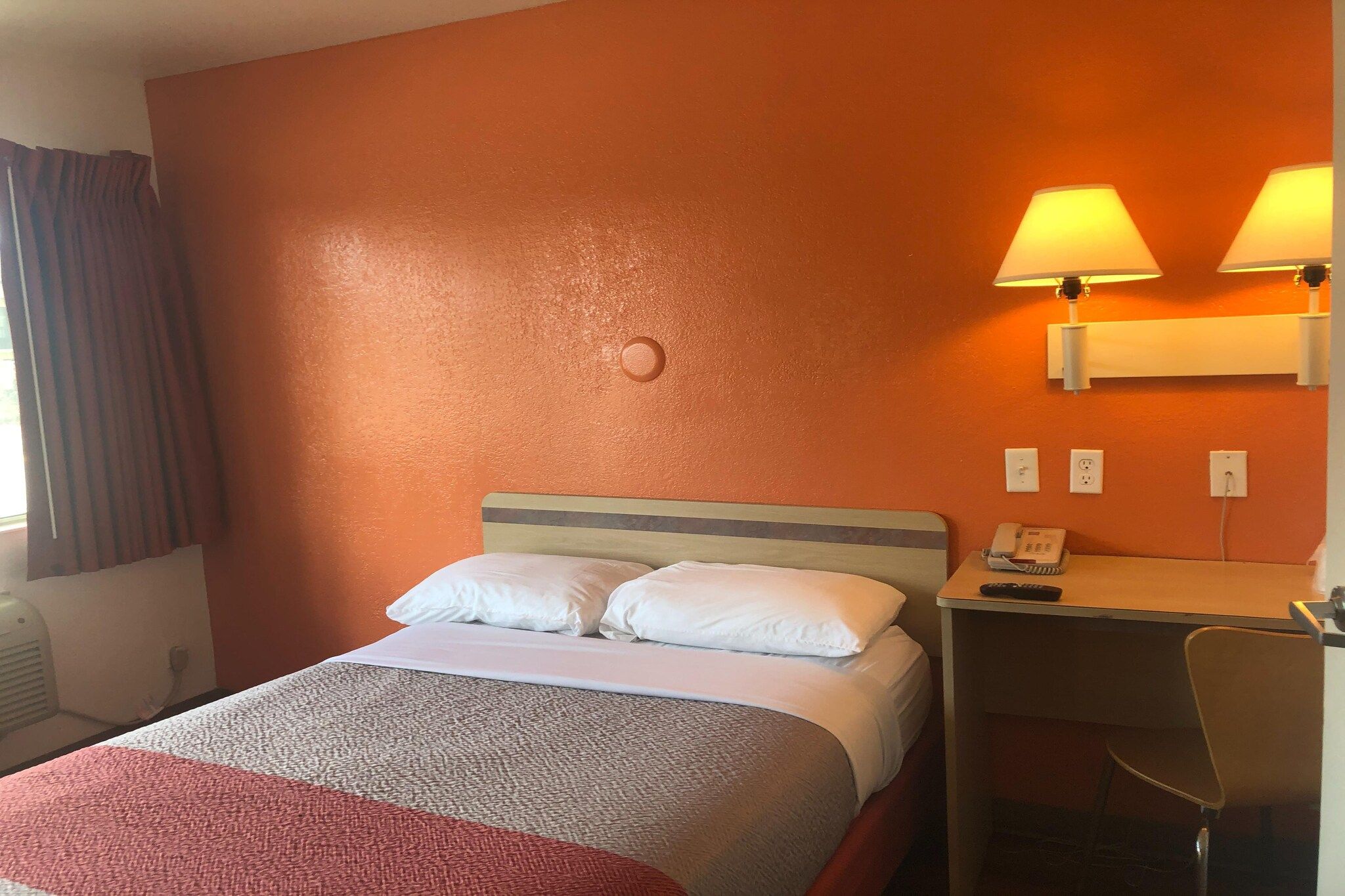 A hotel room with a bed, a desk with a lamp, and a chair.