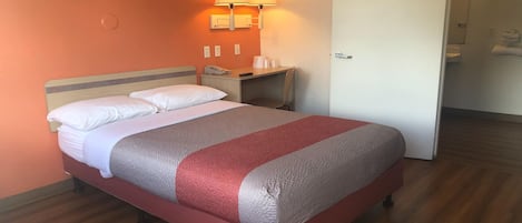A hotel room with a bed, a nightstand, two wall-mounted lamps, a door, and a wooden floor.