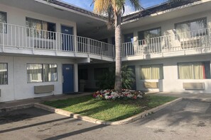 A two-story motel with numbered doors, a central courtyard with a palm tree, and a small flower bed. - Cozy Full Bed Room|Pool|Free Wifi (Jacksonville)