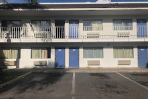 Ein mehrstöckiges Motel mit blauen Türen, nummerierten Zimmern und einem Parkplatz.