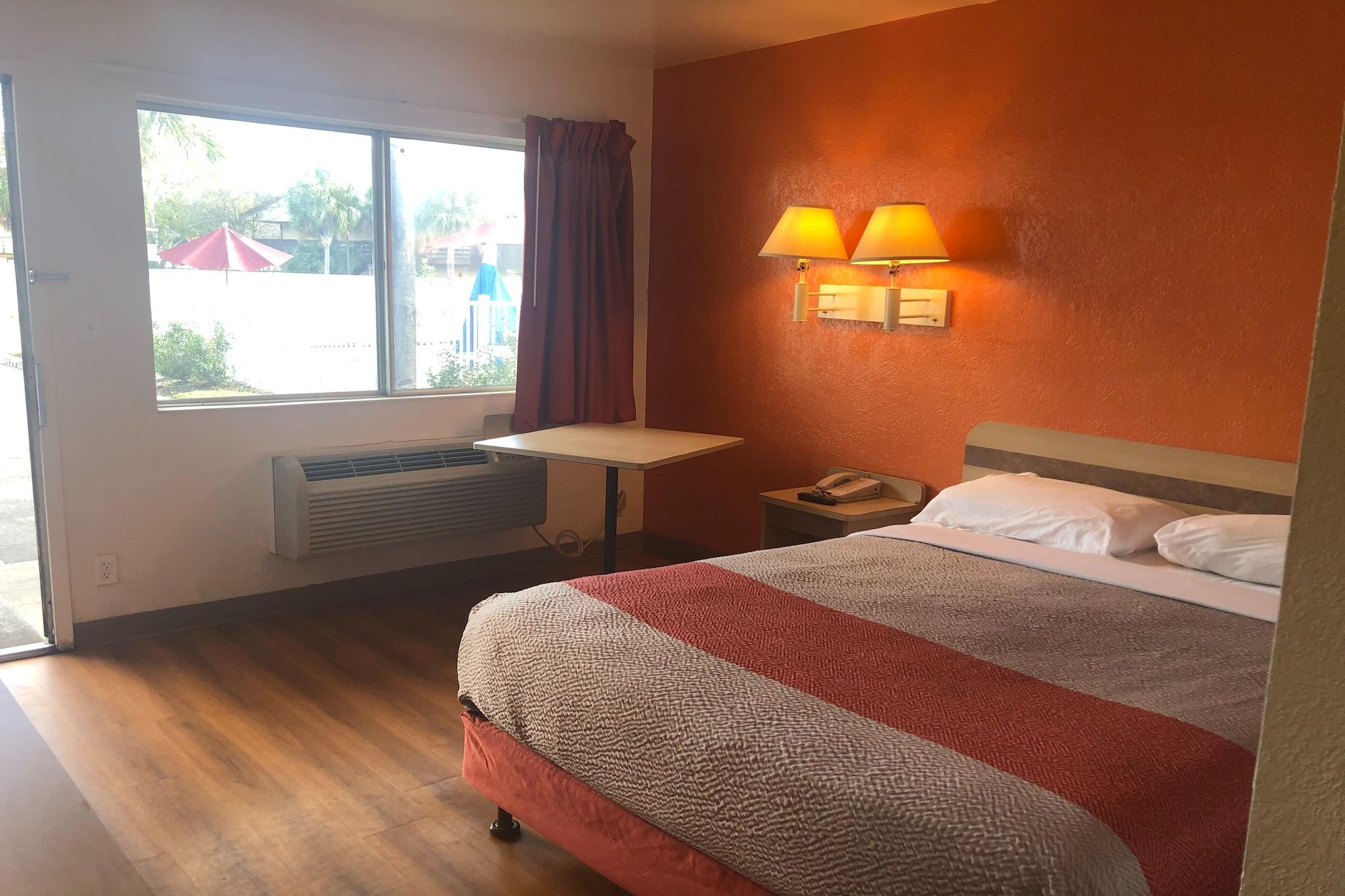 Une chambre d’hôtel avec un lit, une table de chevet, une lampe, une fenêtre avec des rideaux et une vue sur l’extérieur.