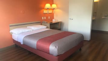 Una habitación de hotel con una cama, una mesita de noche, dos lámparas fijadas a la pared, una puerta y piso de madera.