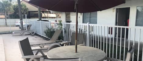 An outdoor seating area with a round table and chairs, a large umbrella, and a white fence.