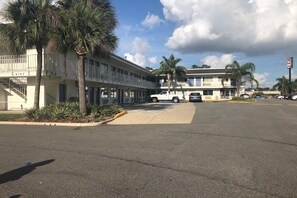 A motel with a parking lot, a white truck, and a palm tree. - 1 Full Bed | ADA/Tub (Jacksonville)