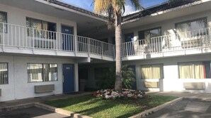 Motel de dues plantes amb portes numerades, un pati central amb una palmera i un petit jardí.