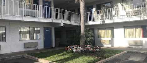 Un motel de dos pisos con puertas numeradas, un patio central con una palmera y un pequeño jardín.