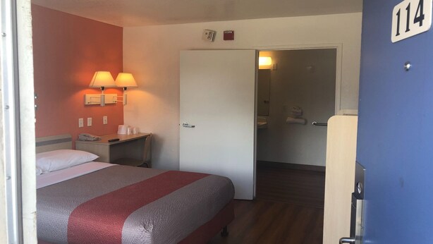 Habitación de hotel con cama, lámparas de noche, escritorio con teléfono y puerta que da a un baño.
