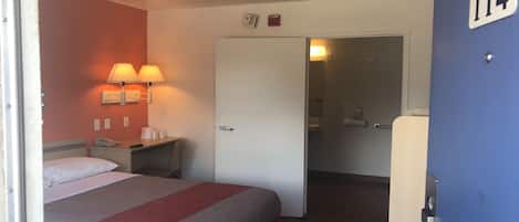 Habitación de hotel con cama, lámparas de noche, escritorio con teléfono y puerta que da a un baño.