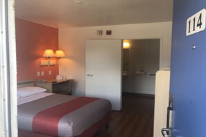 Habitación de hotel con cama, lámparas de noche, escritorio con teléfono y puerta que da a un baño.