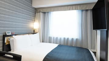 A hotel room with a bed, a bedside table with a lamp, a television, and a window with curtains.