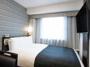 Une chambre d’hôtel avec un lit, une table de chevet avec une lampe, une télévision et une fenêtre avec des rideaux.