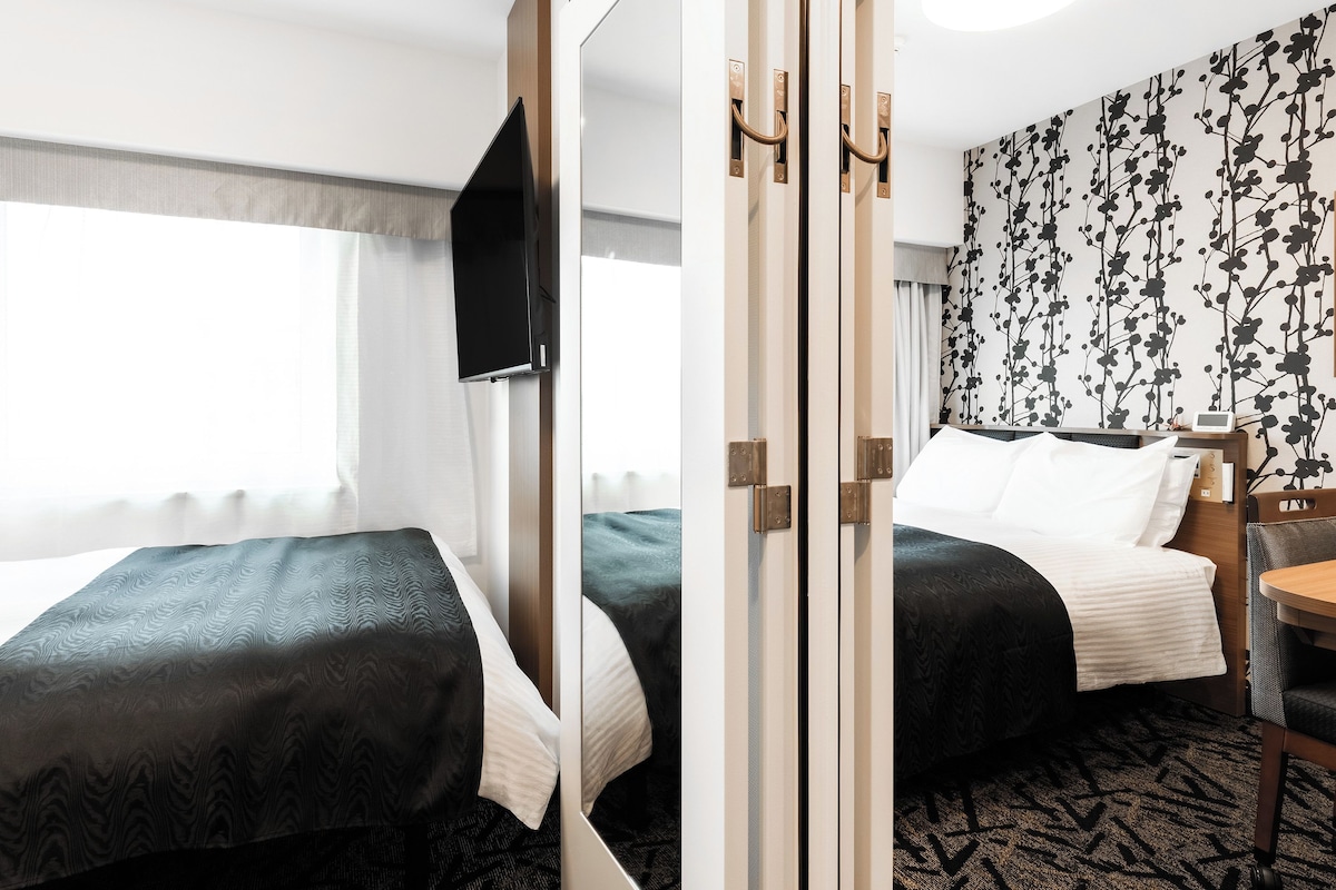 Ein Hotelzimmer mit zwei Betten, einem Fernseher, einem Schreibtisch und einer Wand mit Muster.