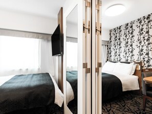 Une chambre d’hôtel avec deux lits, une télévision, un bureau et un mur décoré de motifs.